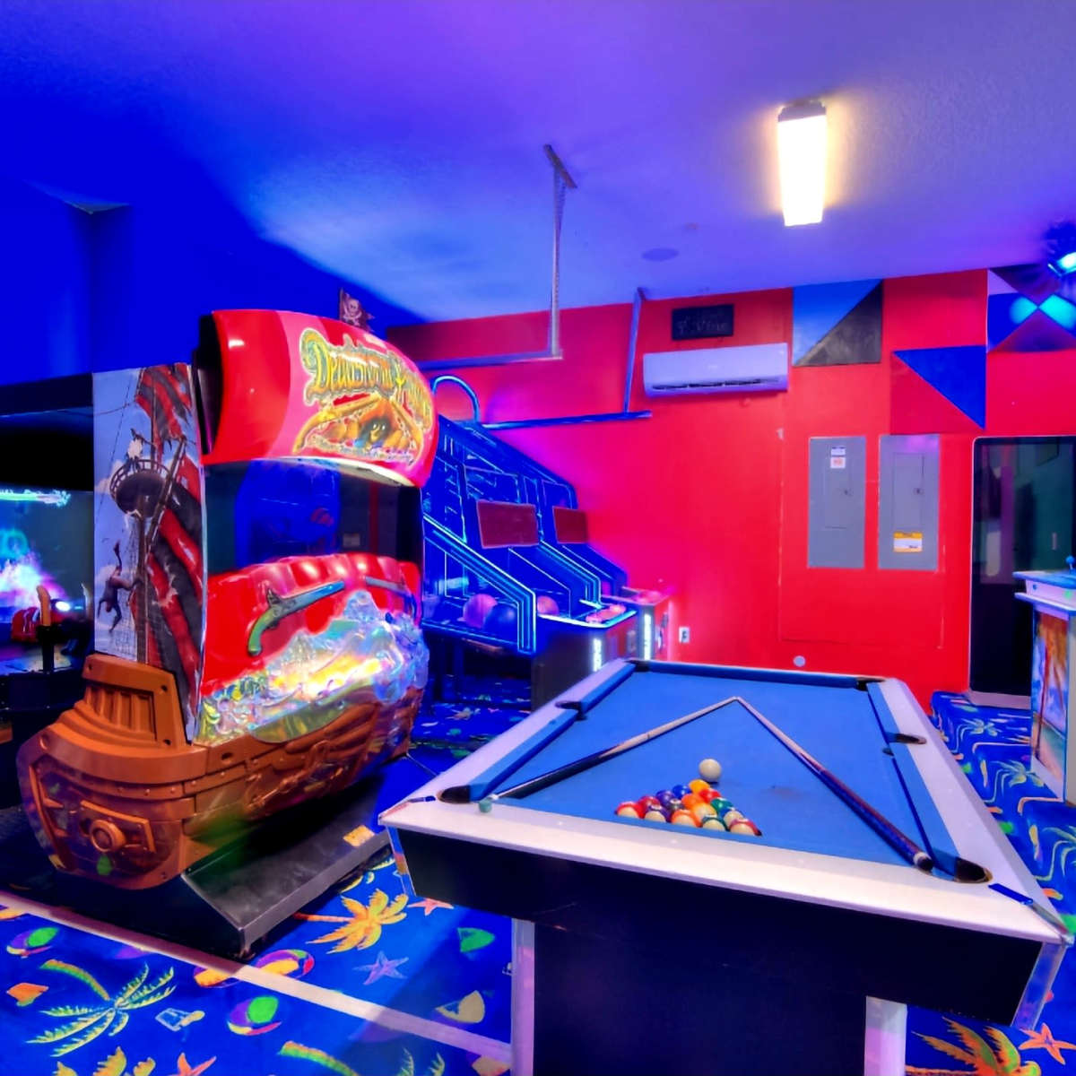 A vibrant arcade room featuring a pirate-themed arcade game and a pool table on a colorful patterned carpet.