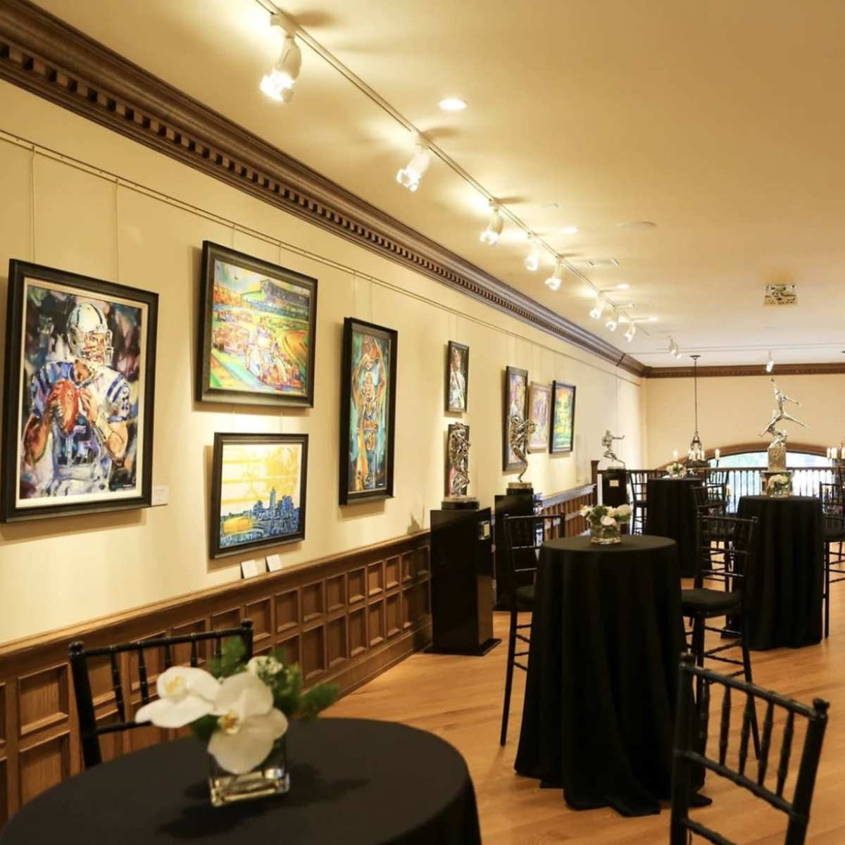 An art gallery featuring a long hallway with framed artworks on the walls and small tables positioned along the sides.