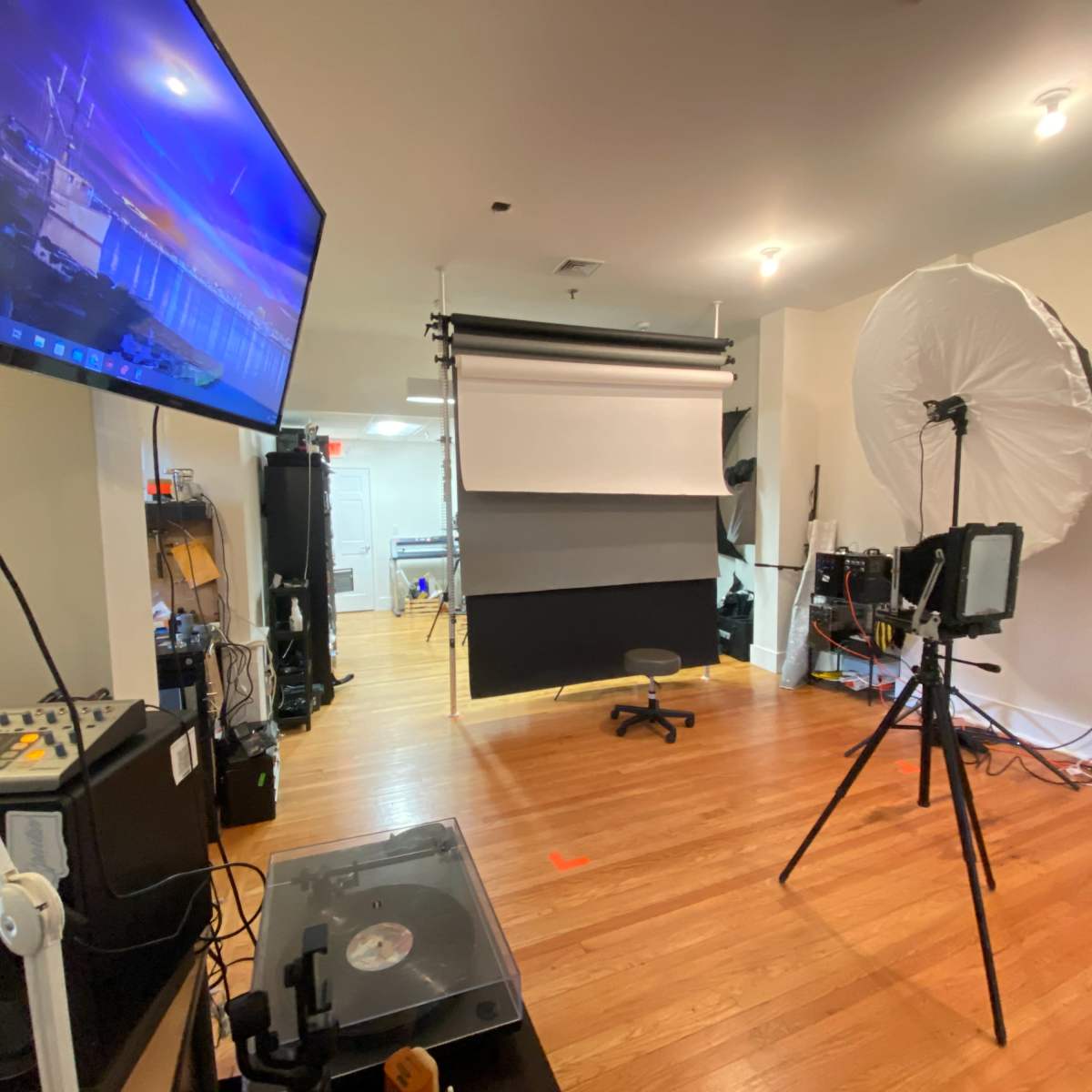 A photography studio is set up with a backdrop, lighting equipment, and a computer monitor displaying an image.