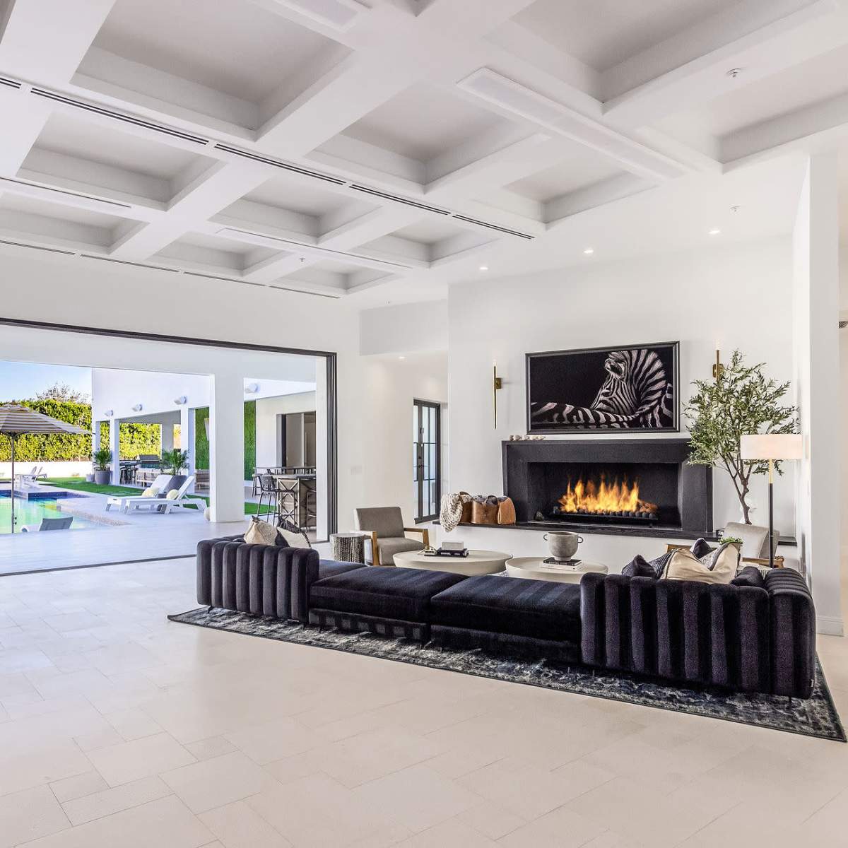 A modern living room with a large sectional sofa and a fireplace, leading to an outdoor pool area through expansive sliding glass doors.