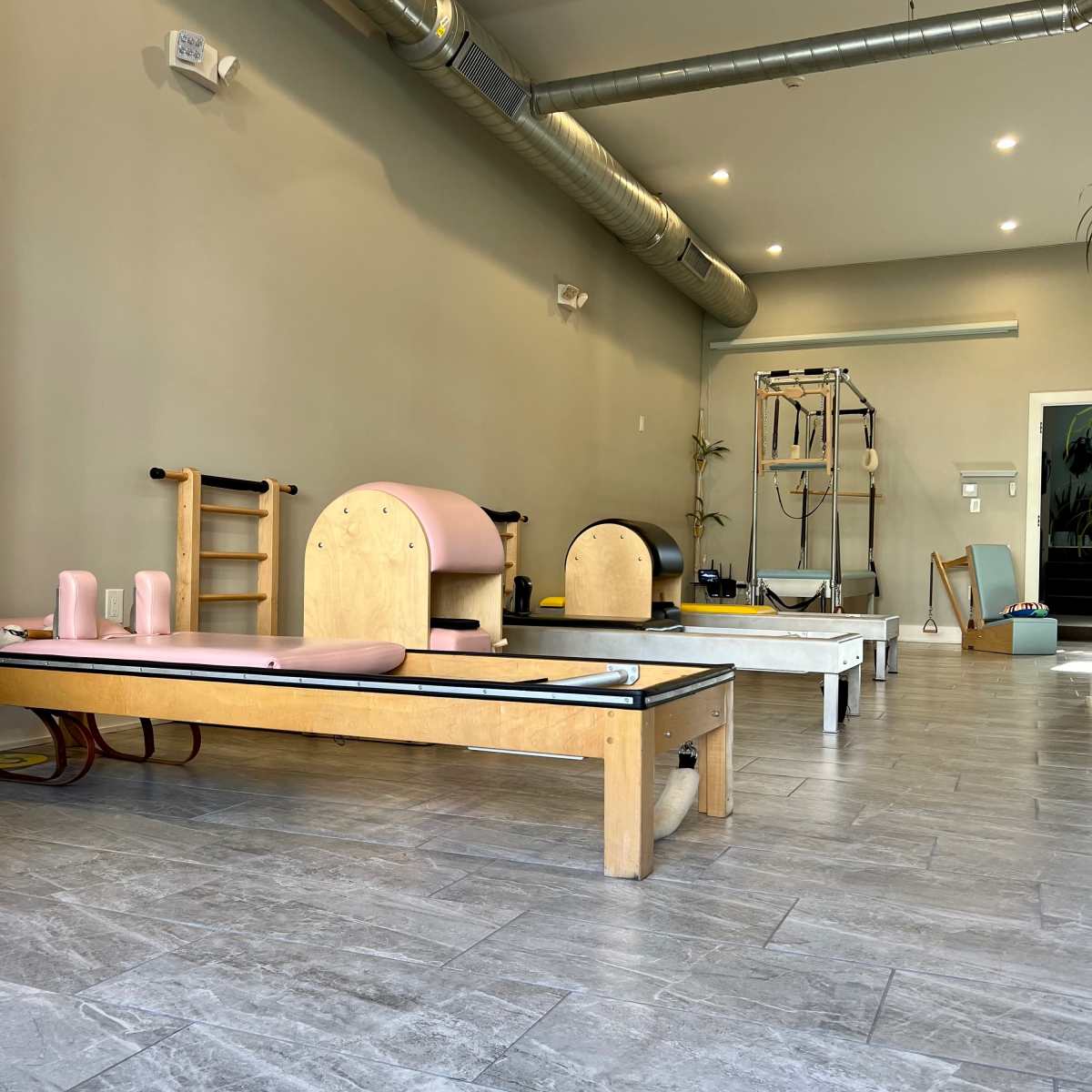 A spacious Pilates studio with wooden reformers and equipment arranged neatly on gray tiled flooring.