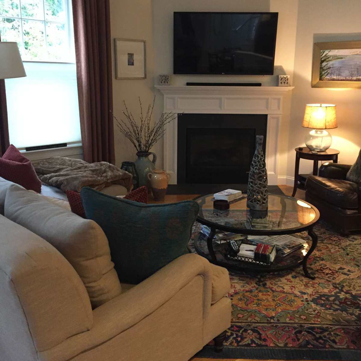The living room features a beige sofa, an armchair, and a coffee table centered in front of a fireplace with a large flat-screen TV mounted above it.