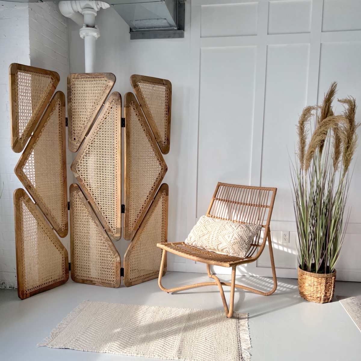 A rattan chair and a decorative screen stand beside a plant in a woven pot on a light-colored floor.