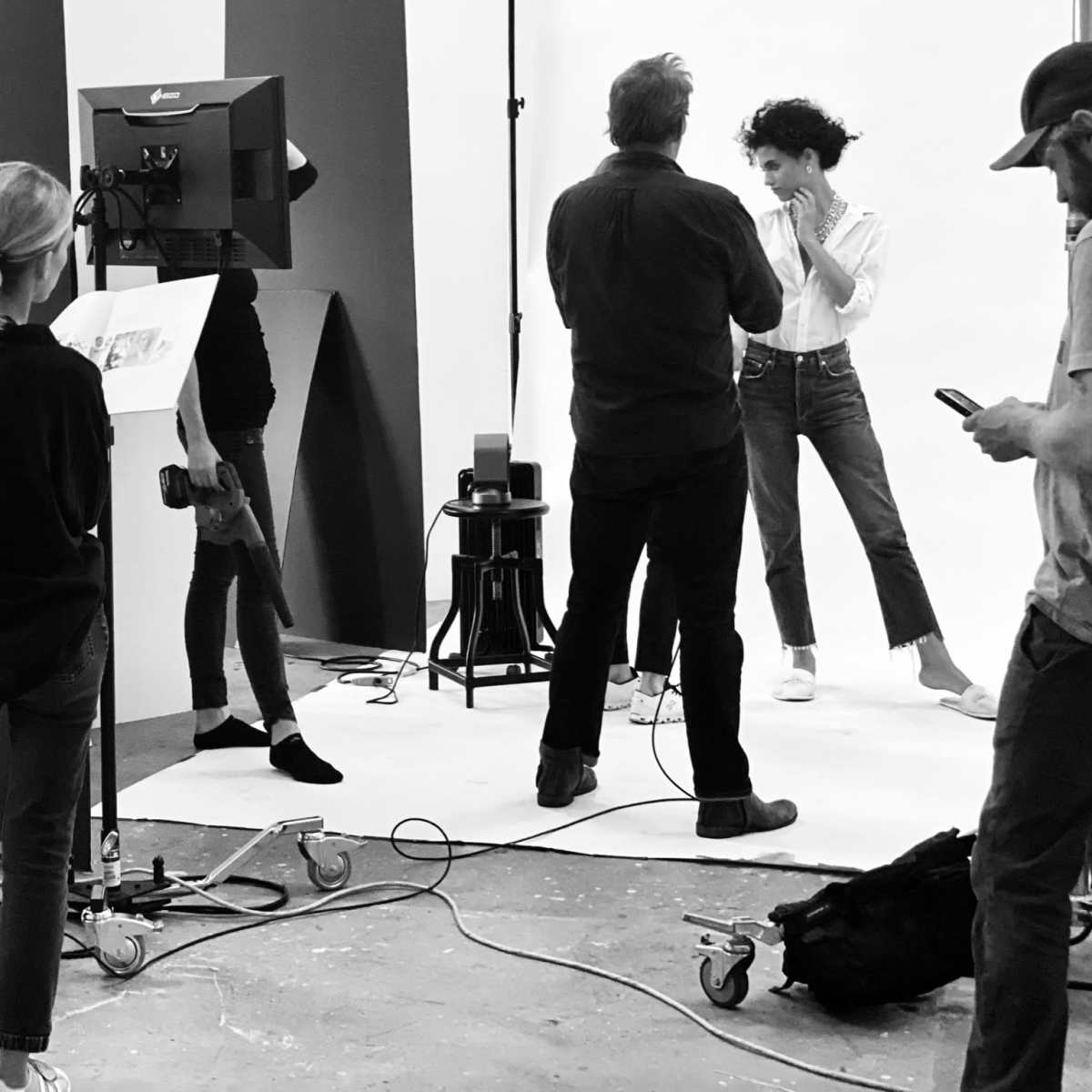 A group of people is working on a photoshoot in a studio, with a model posing in front of a camera while others assist and observe.