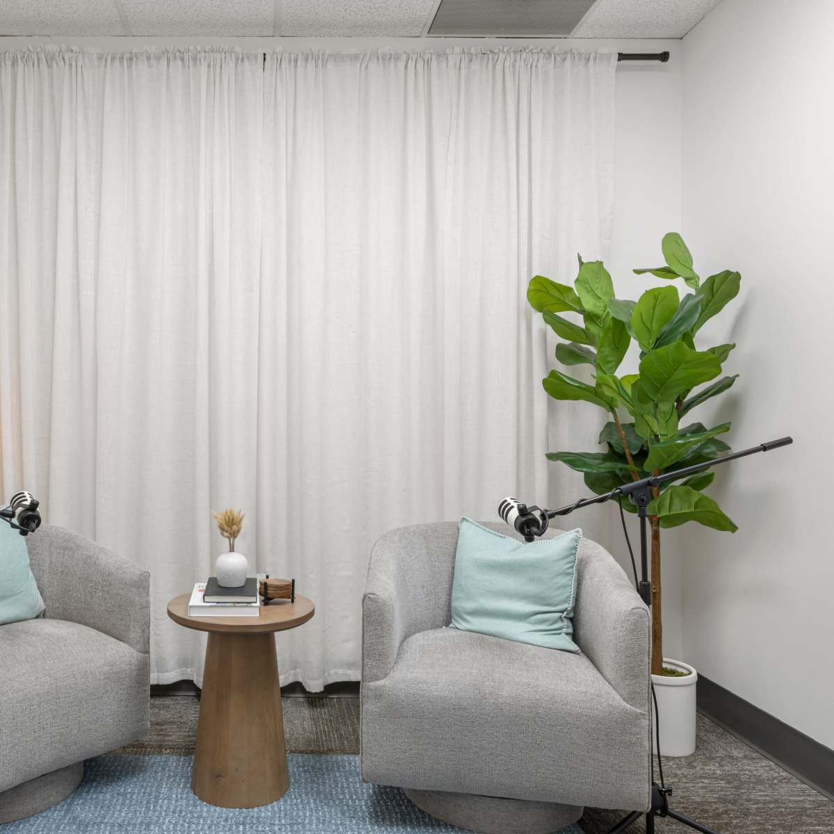 A small, modern space with two gray armchairs, a round wooden table, and a potted plant, all arranged in front of a white curtain.