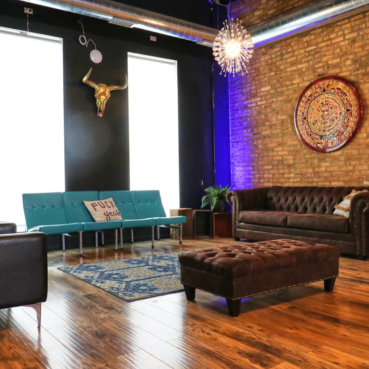 A modern living room with a combination of black leather sofas, a turquoise couch, a decorative rug, and exposed brick walls accentuated by a round wall hanging and a bull skull.