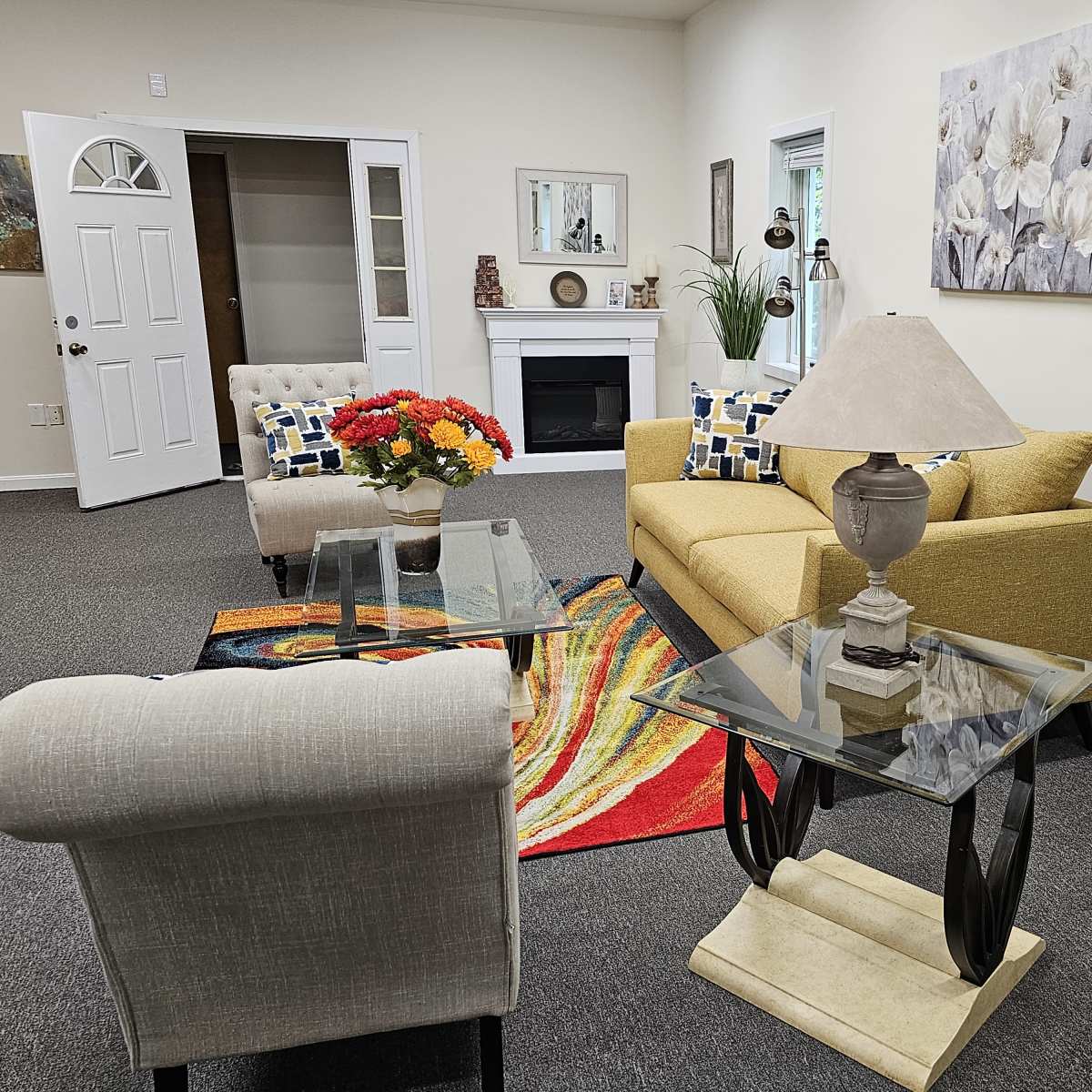 A cozy living area with a yellow couch, glass tables, and a decorative lamp, all arranged on a patterned rug.
