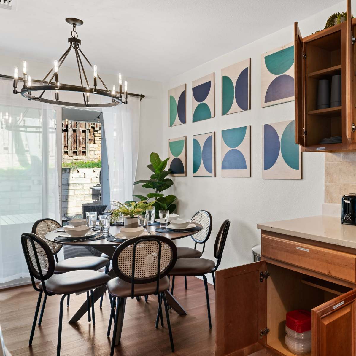 A dining area features a round table set for four, with chairs, and kitchen cabinetry displaying dishes and appliances.