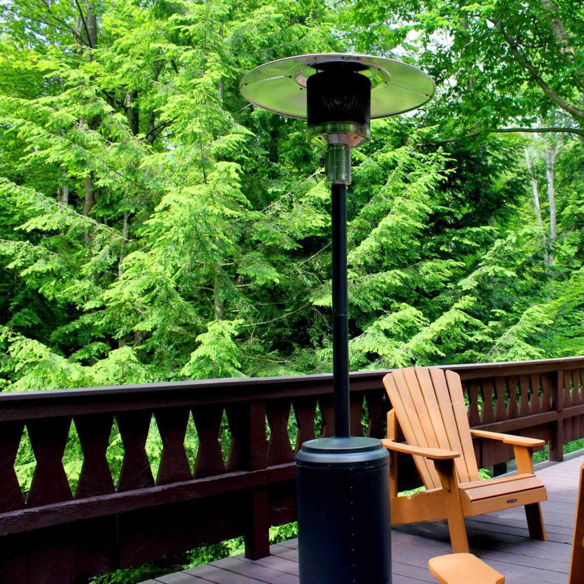 A deck area with wooden furniture and a patio heater overlooks a lush, green forest.