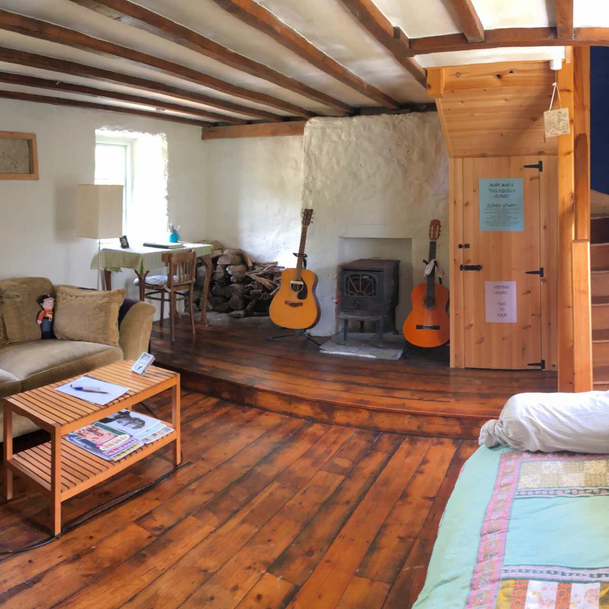A cozy living room with wooden floors, a wood-burning stove, and various musical instruments, including a cello and guitars, arranged throughout the space.