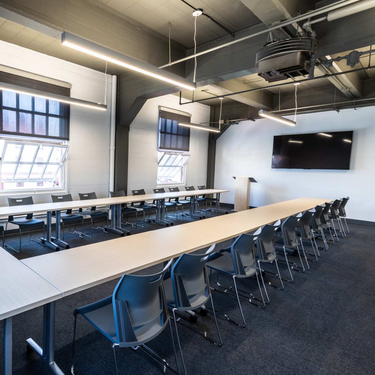 A modern conference room features a long table arranged in a U-shape with gray chairs and large windows.