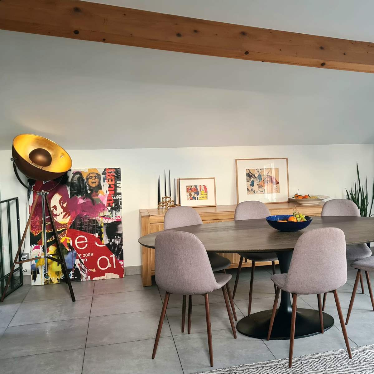 A modern dining area features a round table surrounded by six gray chairs, accompanied by a wooden sideboard and colorful artwork on the walls.