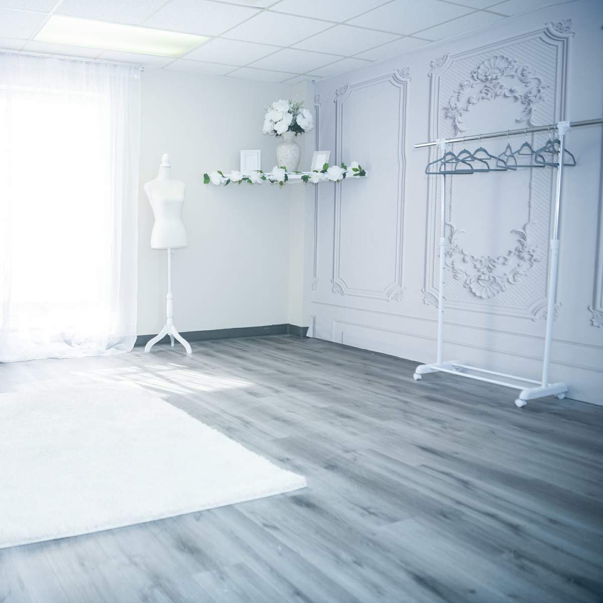 The room features a light-colored floor, a white decorative wall, a mannequin, a clothing rack, a bench, and a fluffy rug.