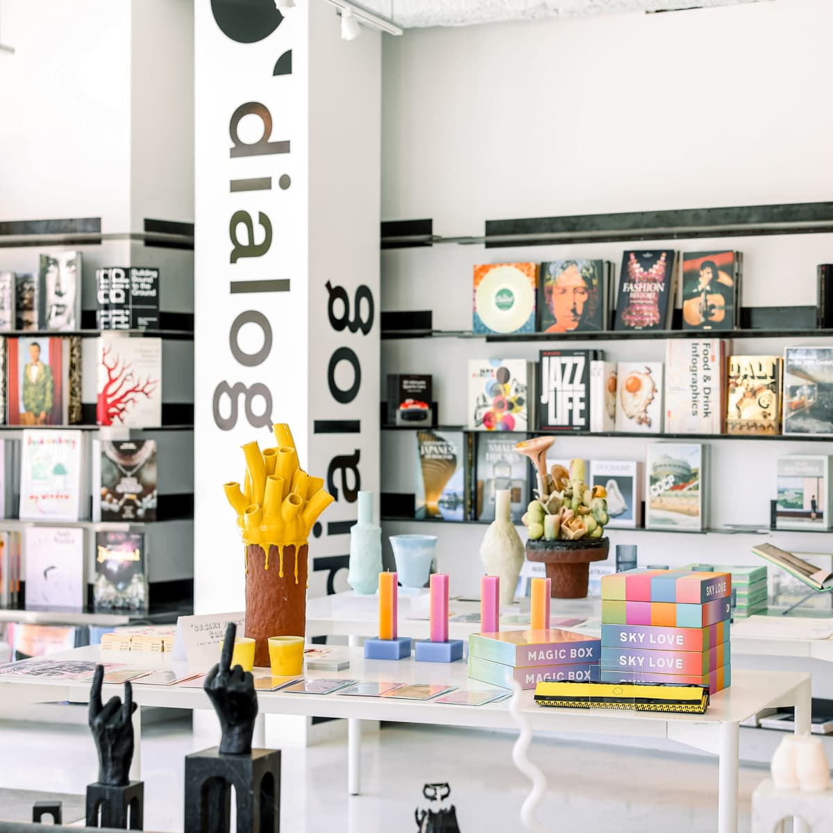 A modern retail space featuring colorful bookshelves filled with various publications and a white table displaying artistic objects.