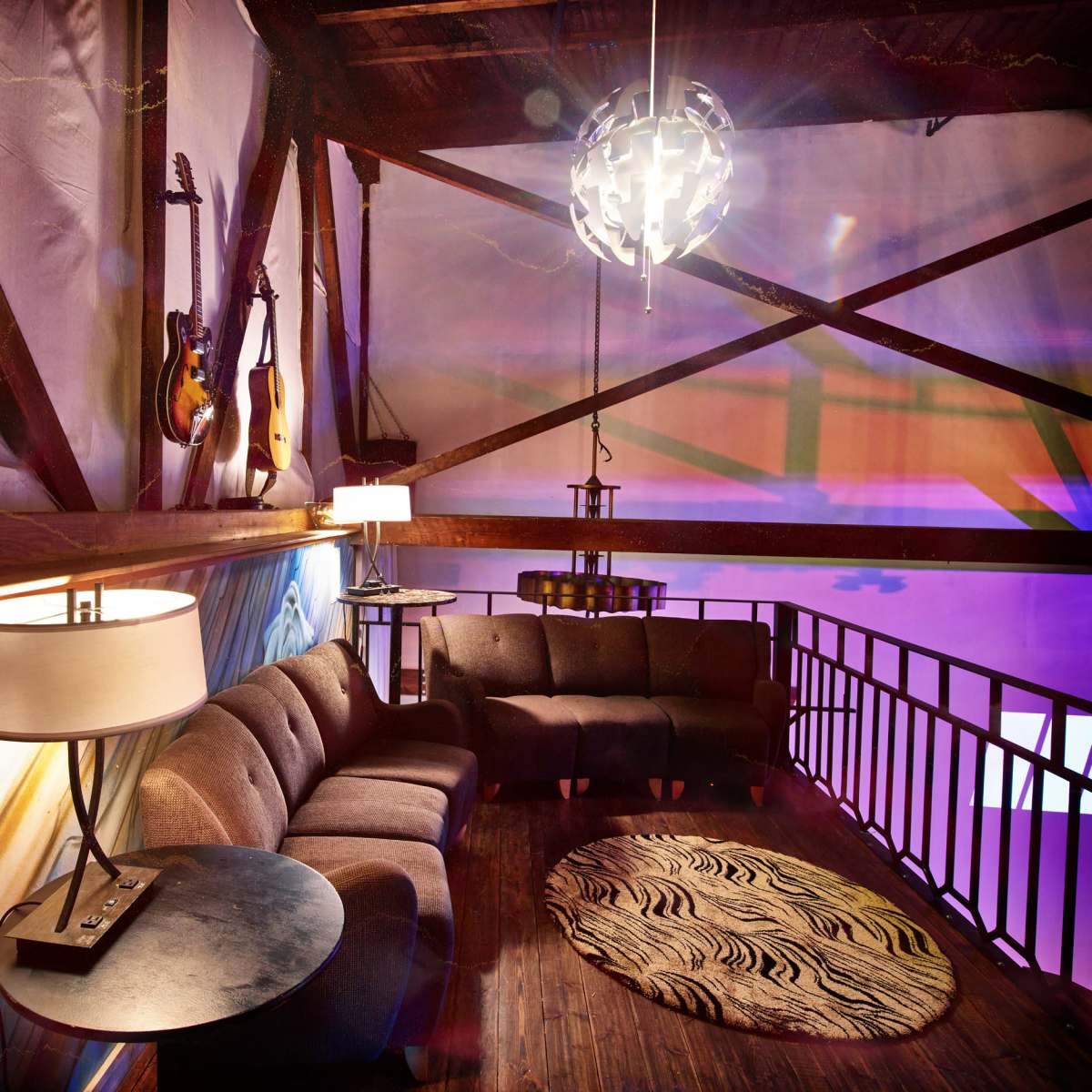 A cozy lounge area with a curved sofa, a round rug, and guitars displayed on the walls, illuminated by modern lighting fixtures.