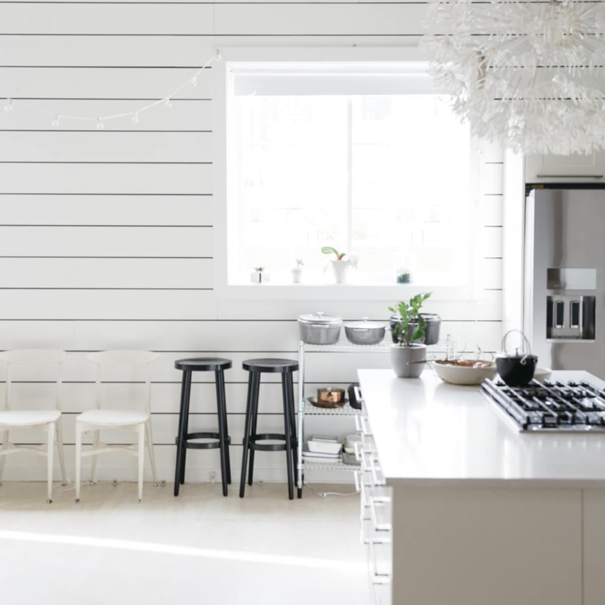 A bright kitchen features a large window, white shiplap walls, contemporary bar stools, and a modern gas stove with an island.