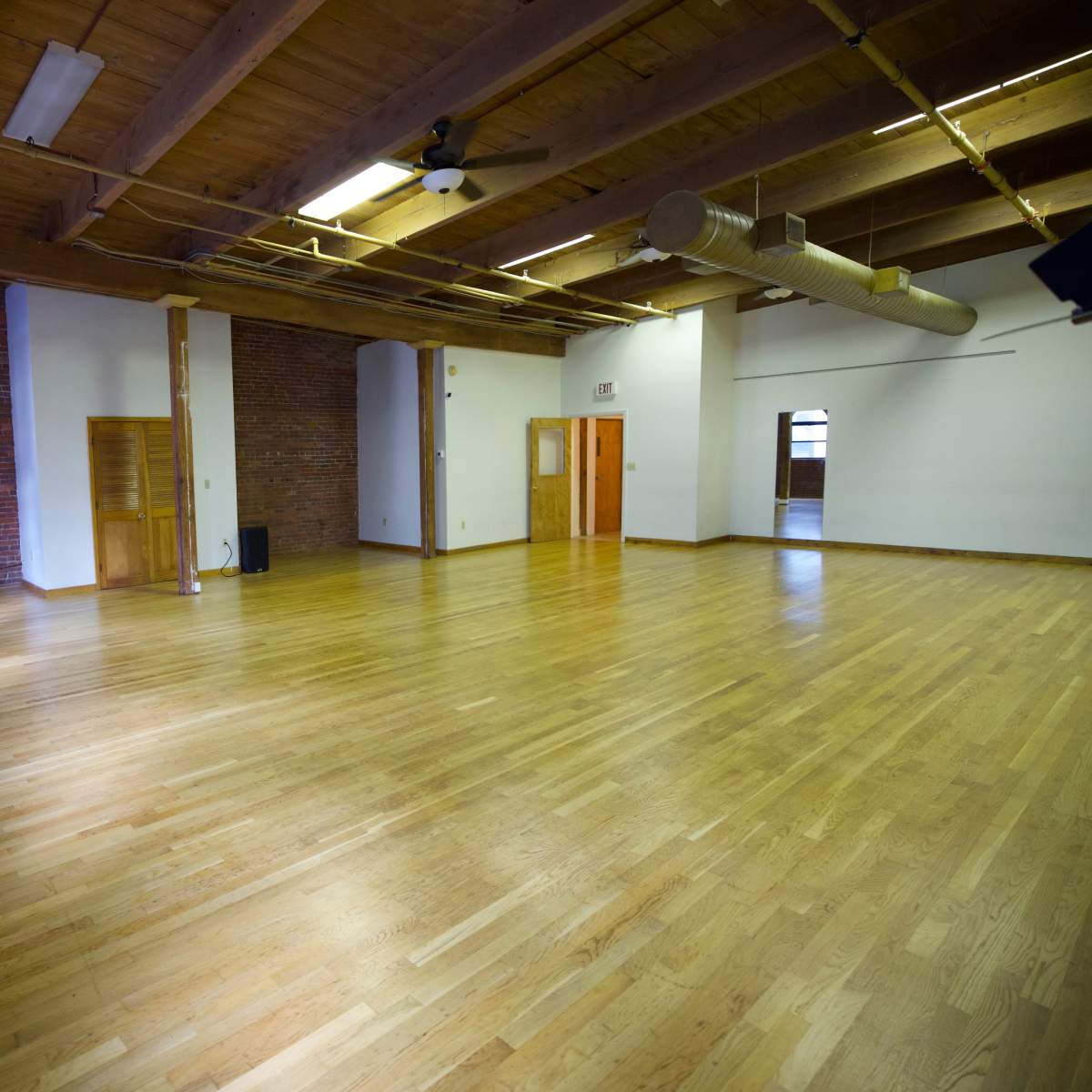 A spacious, empty wooden-floored room with exposed brick walls and large windows.