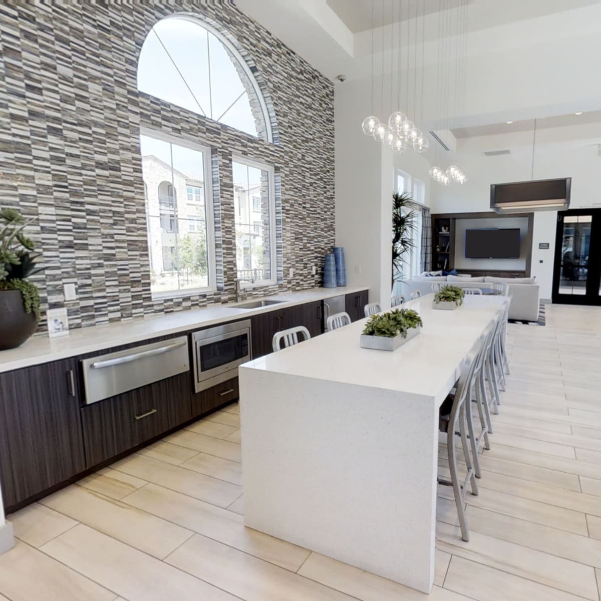 A modern kitchen with a long countertop, stainless steel appliances, and large windows letting in natural light.