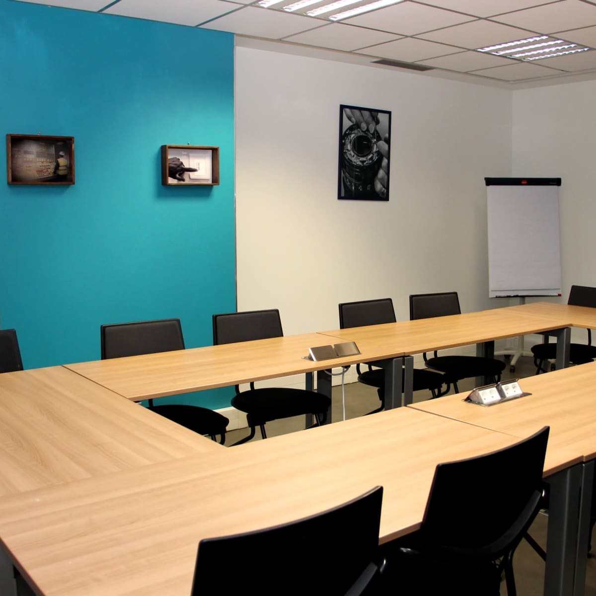 A conference room features a large, rectangular wooden table surrounded by black chairs, with blue accent walls and framed pictures hung on the walls.