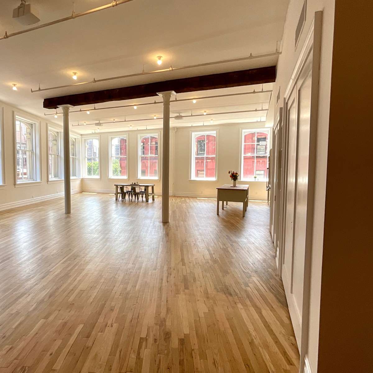 A bright, spacious room with large windows, hardwood flooring, and minimal furnishings including a sofa and a table.