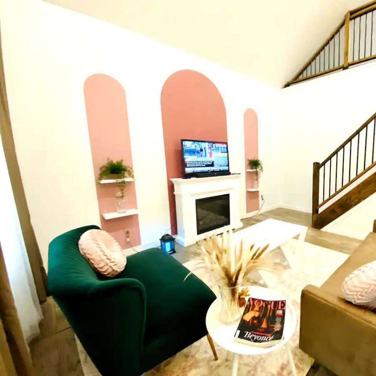 A modern living room featuring a television above a white fireplace, two sofas in contrasting colors, and a staircase in the background.