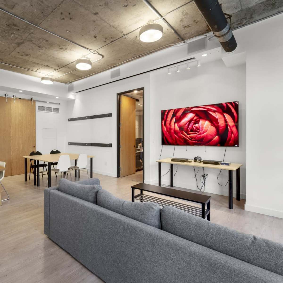 A modern living space featuring a gray sofa, a wooden dining table, and a large TV mounted on a wall displaying a close-up of a red rose.