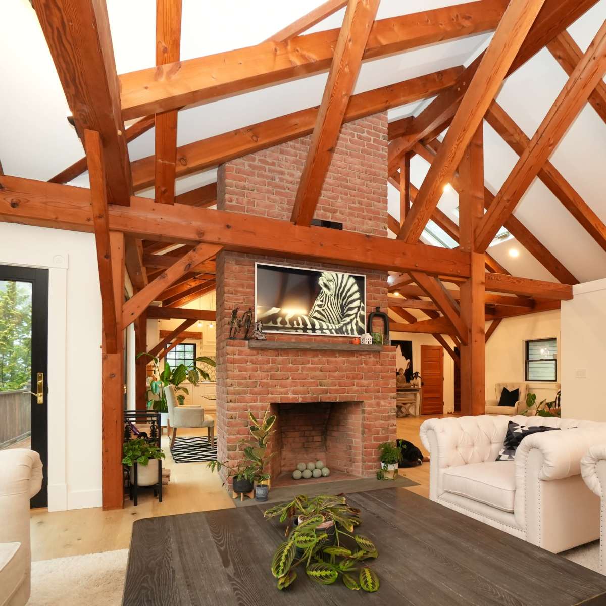 A living room with exposed wooden beams, a brick fireplace, and two white upholstered sofas, all arranged around a central table.