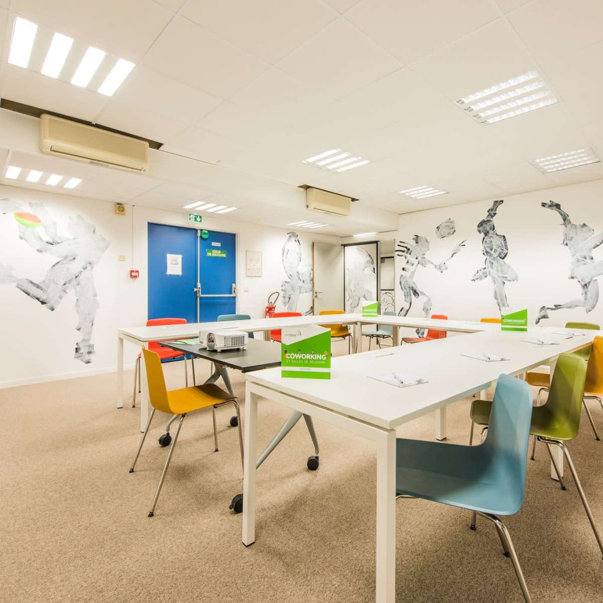 A modern meeting room with a long white table surrounded by colorful chairs and mural-style artwork on the walls.