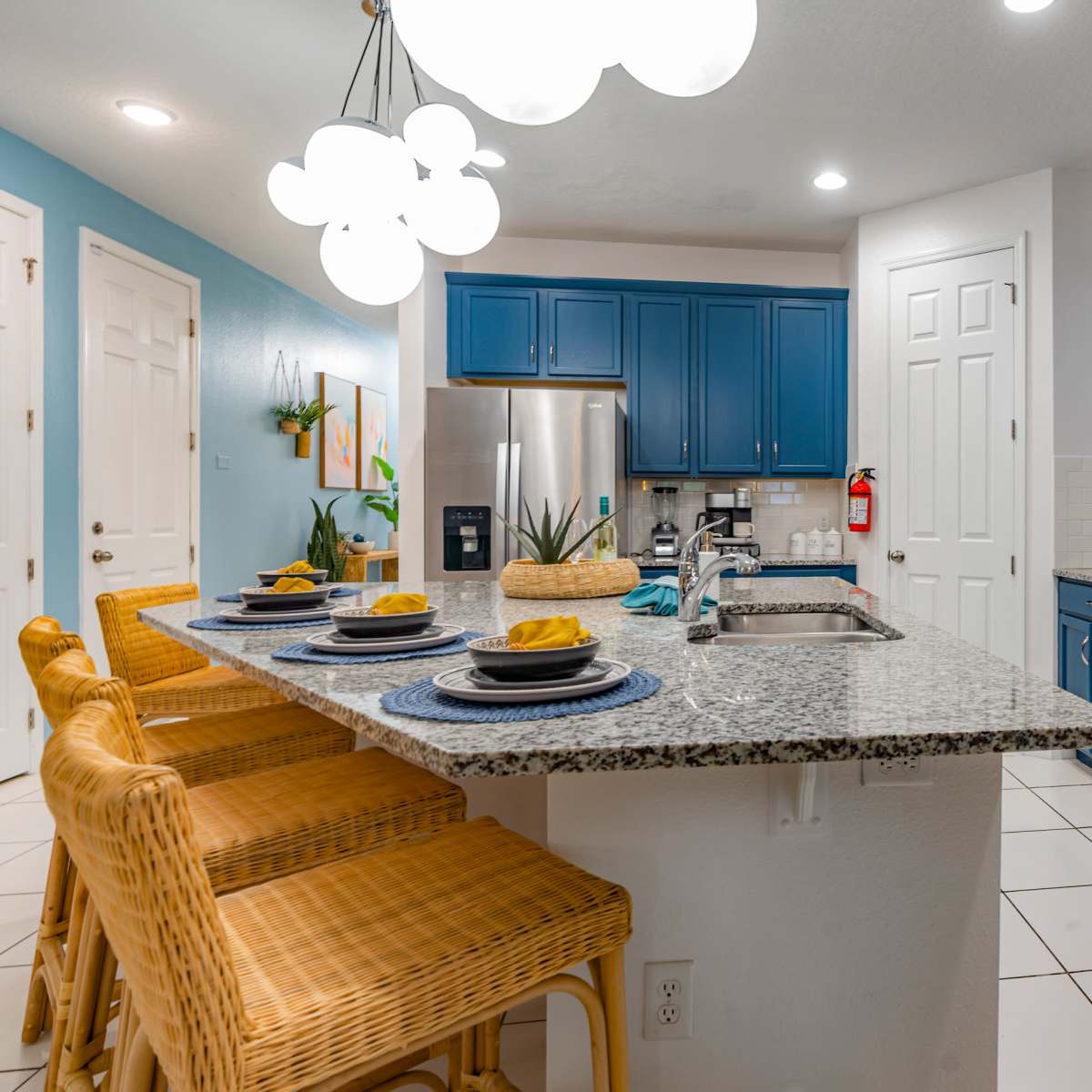 A modern kitchen featuring blue cabinets, a granite countertop with bar stools, and stainless steel appliances.