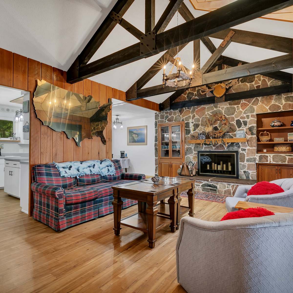 The living room features a stone fireplace, wooden beams, and a plaid sofa with a wooden coffee table.