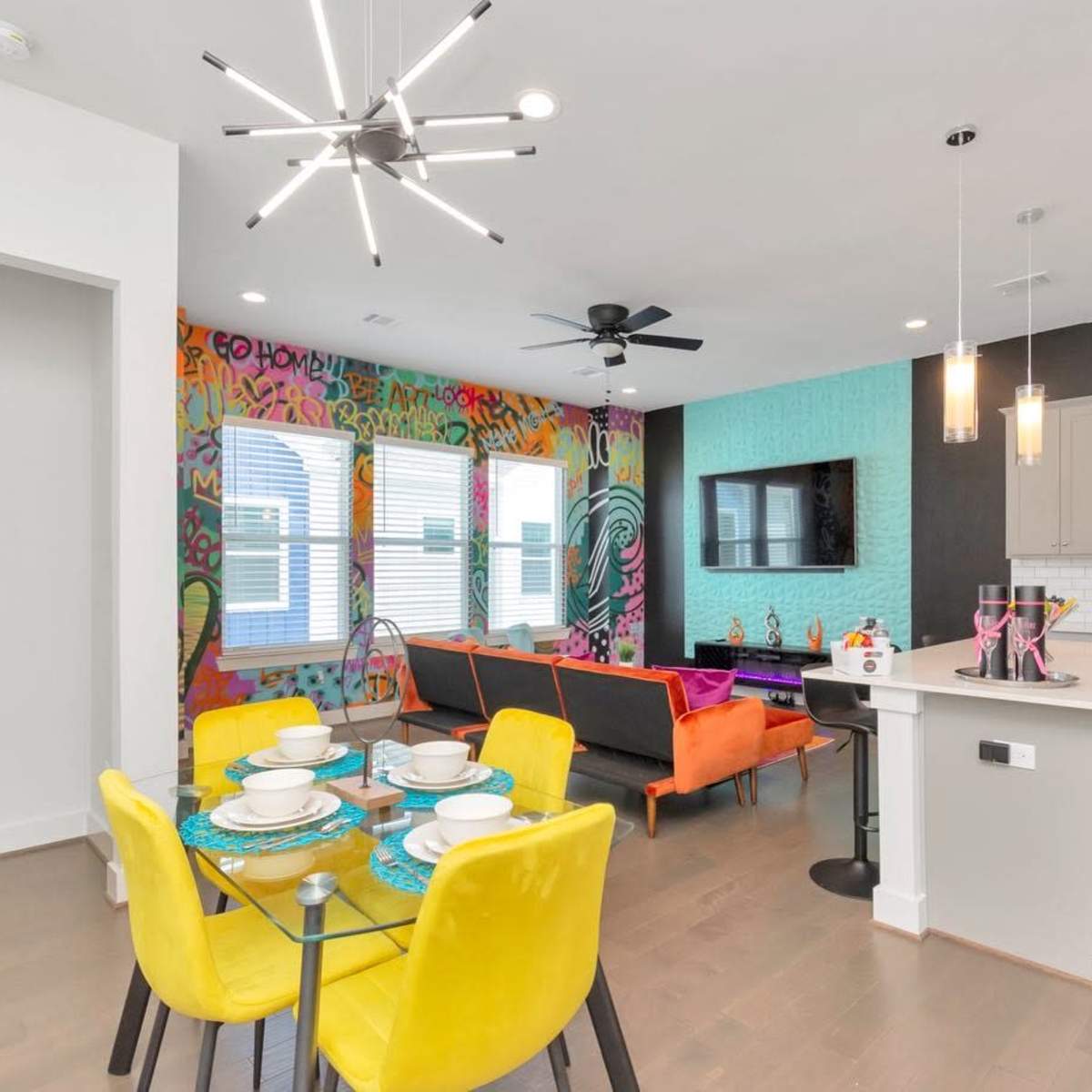 A modern open-concept living and dining area with vibrant wall art, a table set for dining, and colorful furniture arrangements.