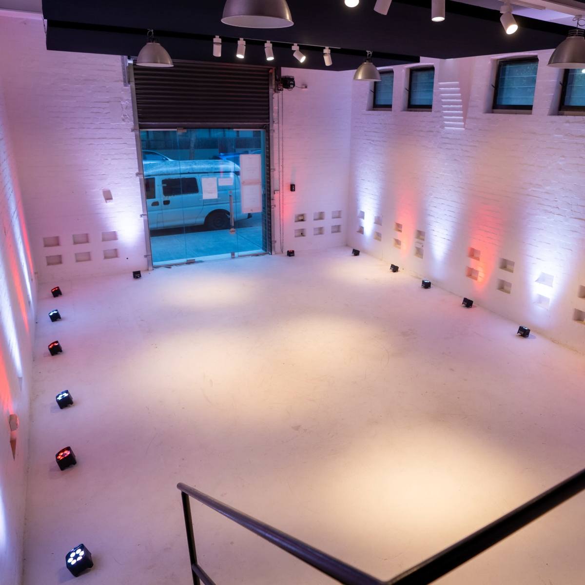 A spacious, well-lit room with white brick walls and a concrete floor, featuring multiple colored lights positioned along the perimeter.