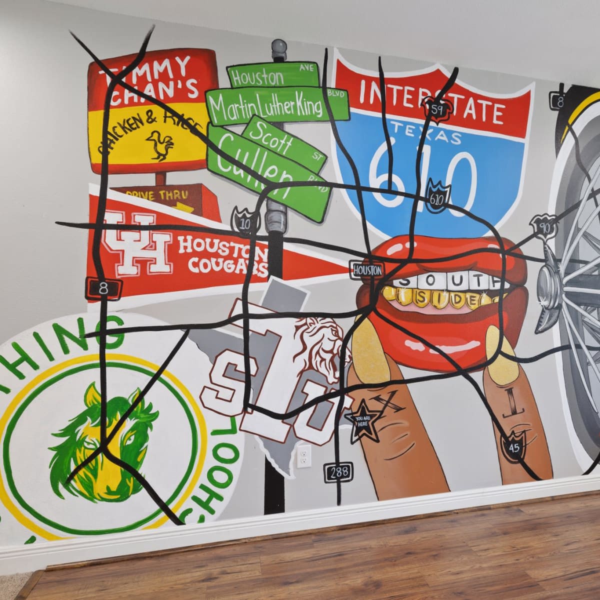 A large mural on a wall, depicting a bicycle wheel adorned with street signs and symbols representing various locations and schools.