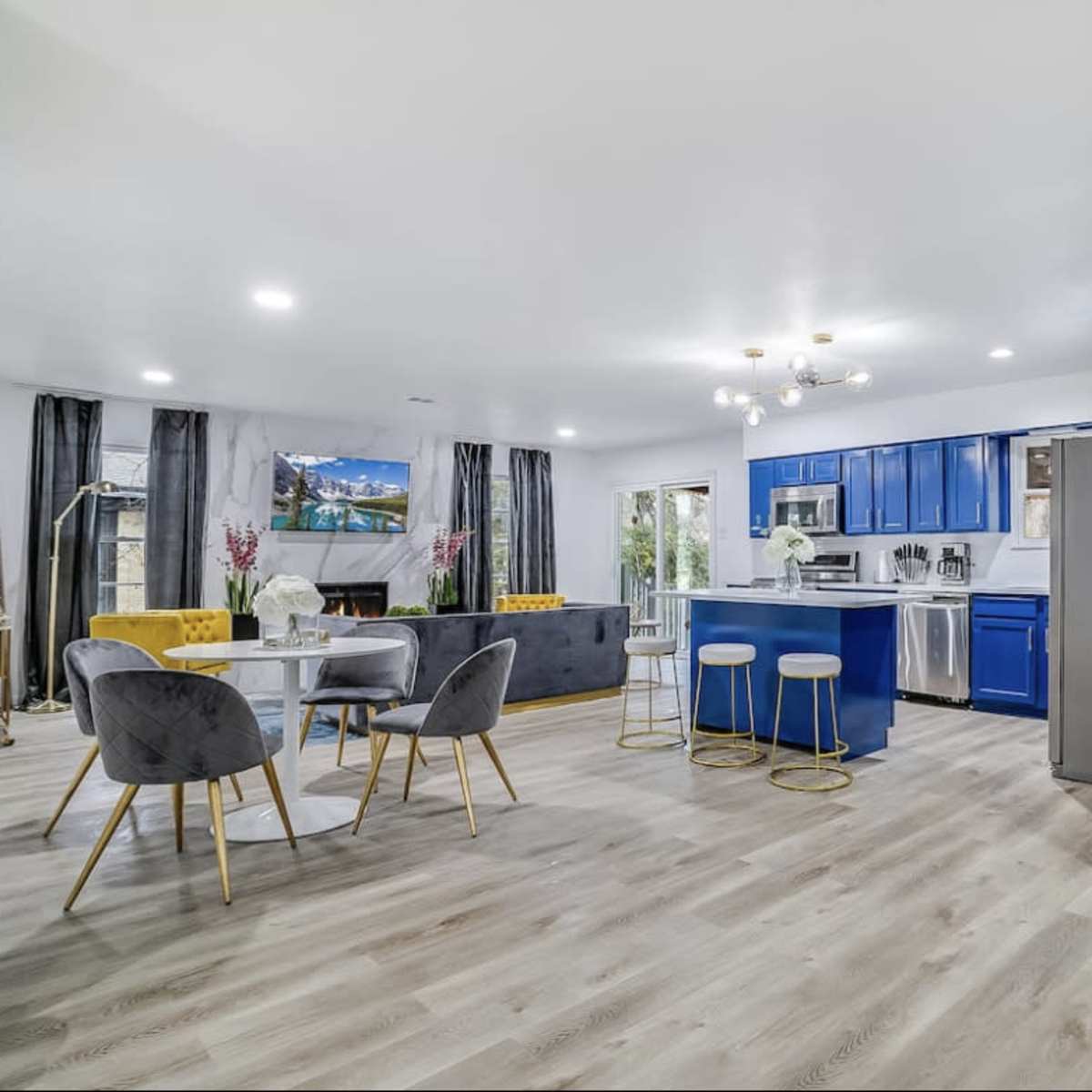 A modern kitchen and dining area featuring blue cabinetry, a round dining table, and a green wall with the word "good vibes."