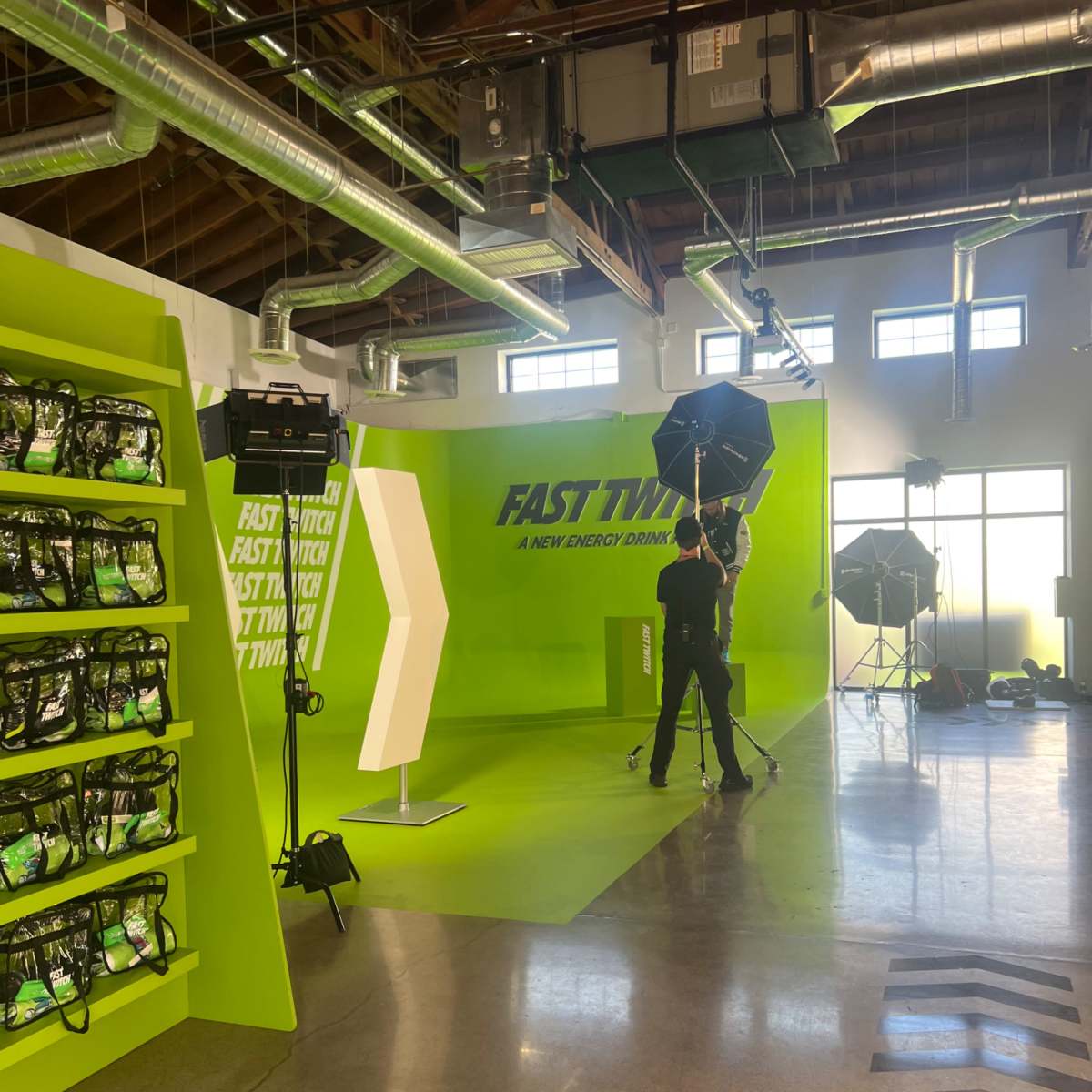 A person is setting up lighting equipment in a brightly colored studio space featuring a green backdrop and shelves of storage.