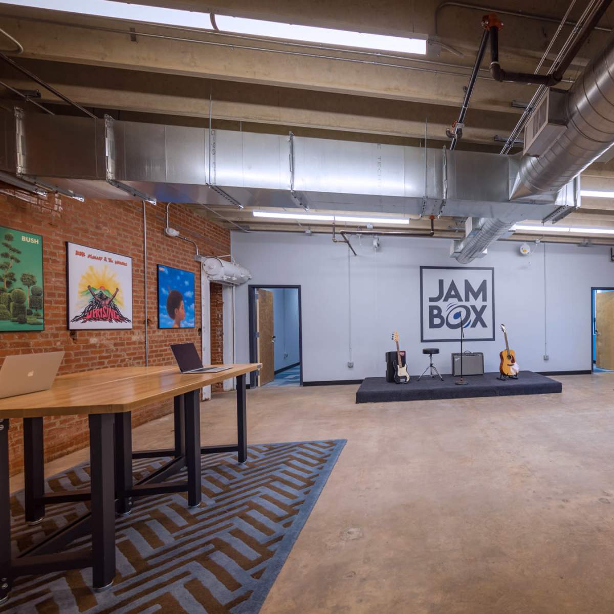 A spacious room with brick walls, a performance stage at the center featuring two guitars, and various art pieces on the walls.