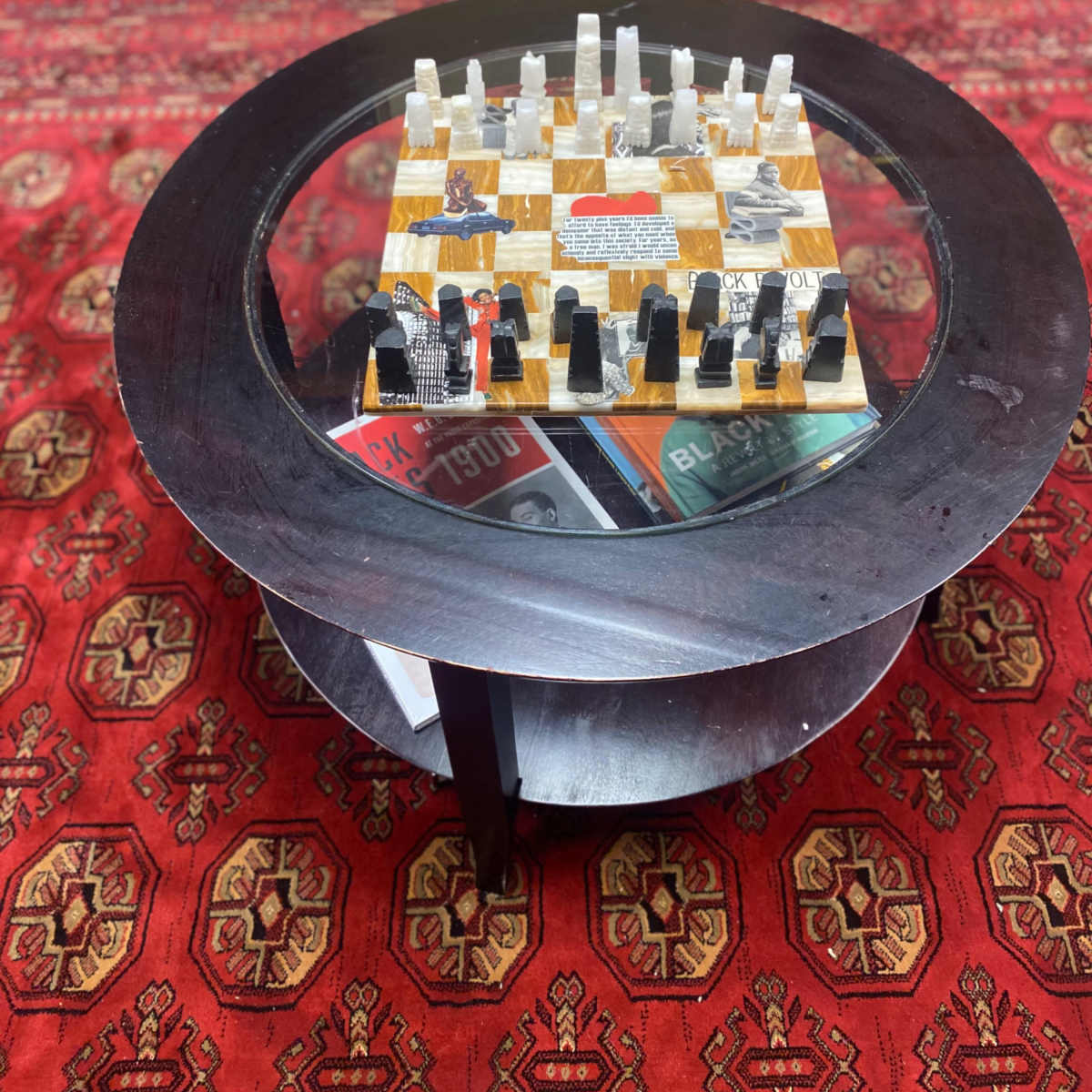 A glass-topped table displays a chessboard set with black and white pieces on a patterned red rug.