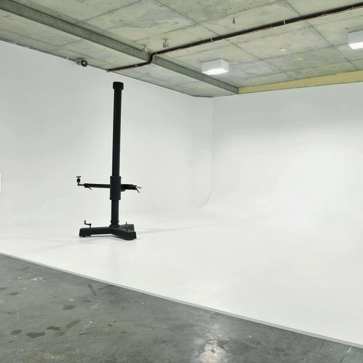 An empty studio space with a seamless white backdrop and a backdrop support stand in the center.