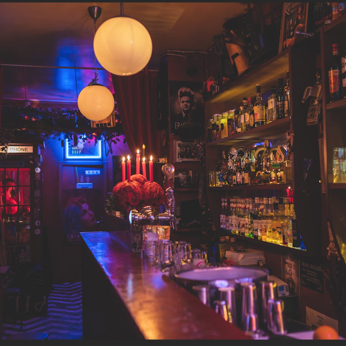A dimly lit bar features shelves stocked with various bottles, illuminated by soft lighting and candlelight.