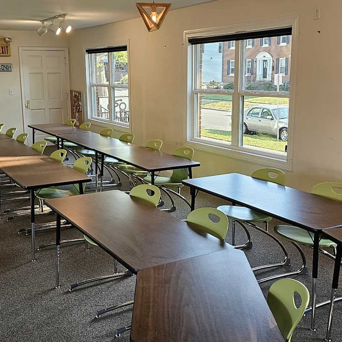 A classroom setup with several rows of tables and chairs, illuminated by natural light from windows.