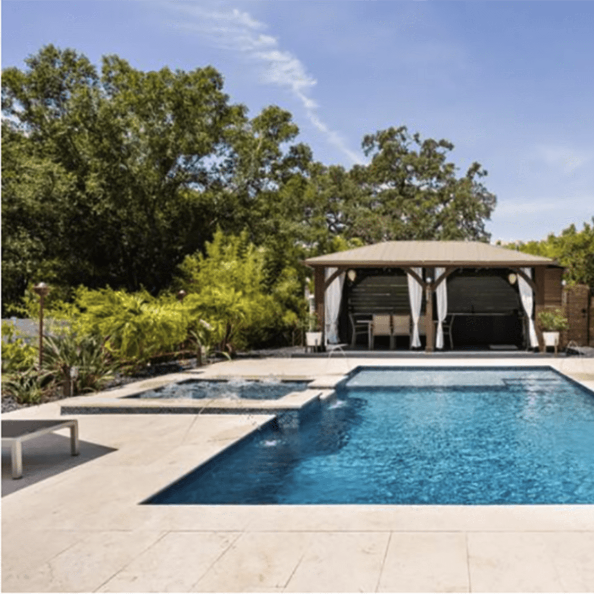 A tidy backyard featuring a swimming pool with surrounding lounge areas, a gazebo, and steps leading up to a house.