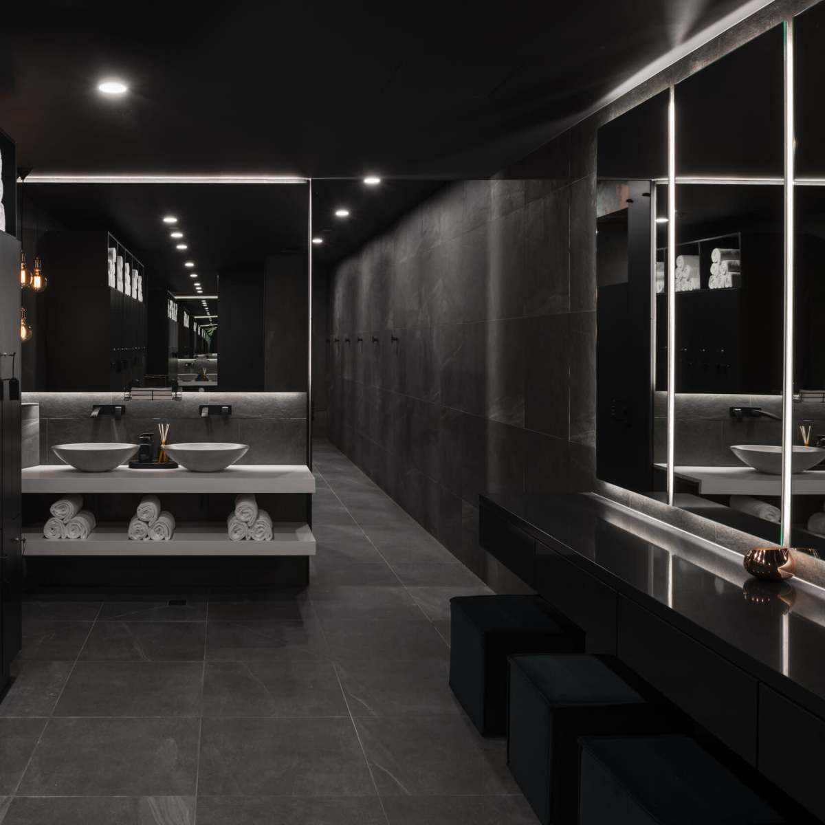 A modern bathroom with dark walls, dual sinks, and neatly arranged towels on shelves.