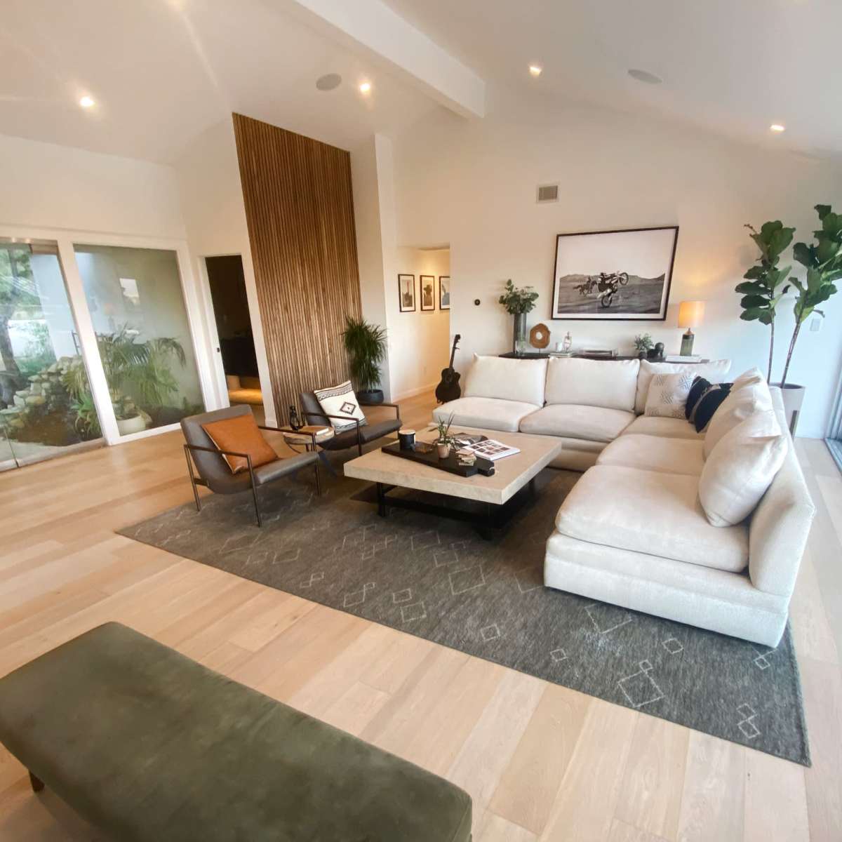 A spacious living room with a large sectional sofa, a coffee table, and glass walls that open to an outdoor area.