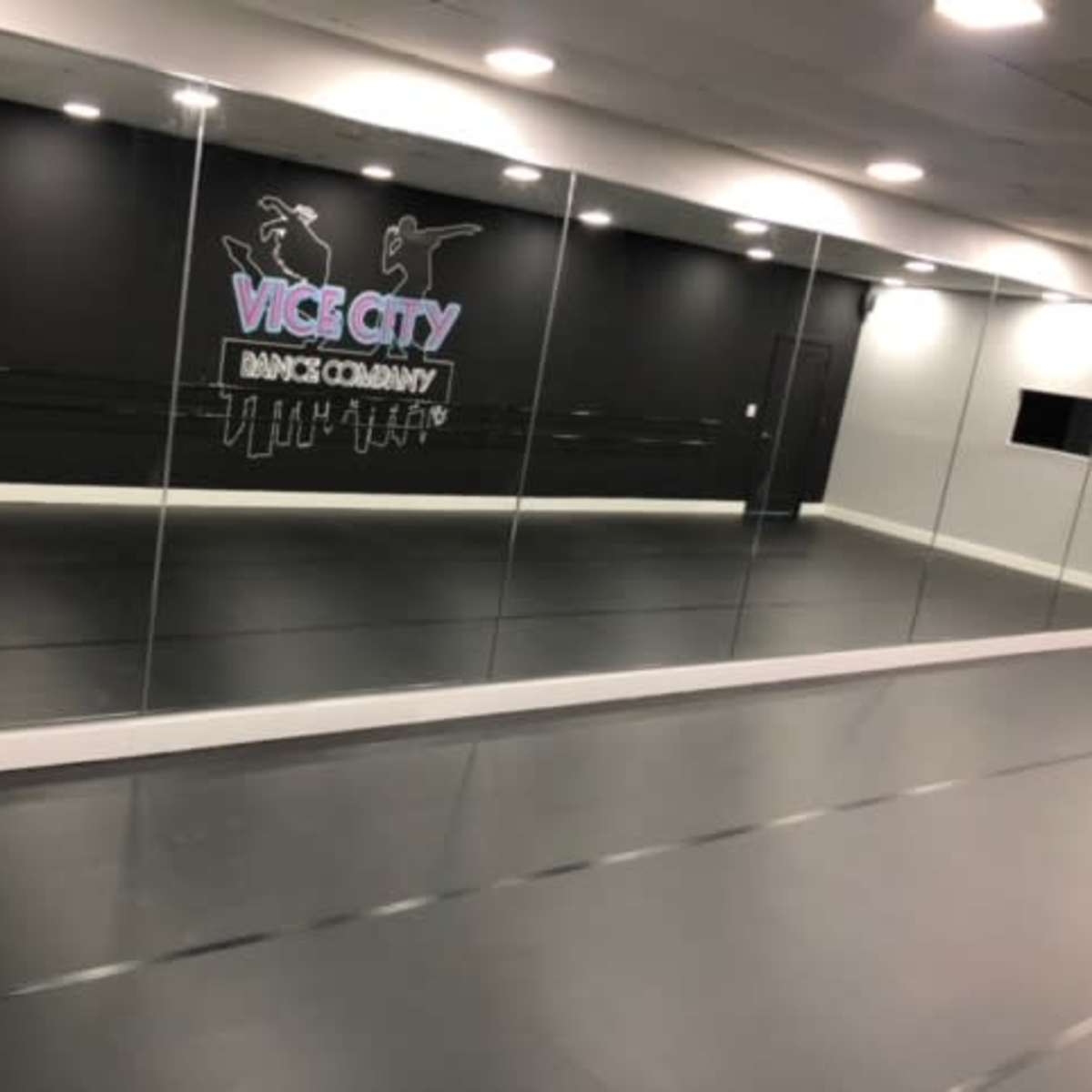 A dance studio with a mirrored wall and a black background featuring the words "VICE CITY DANCE COMPANY" in purple and white.