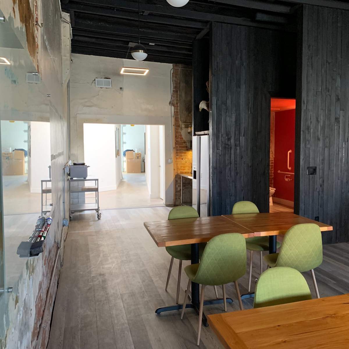 A spacious, modern room features wooden tables and green chairs, with a view of a hallway leading to other rooms.