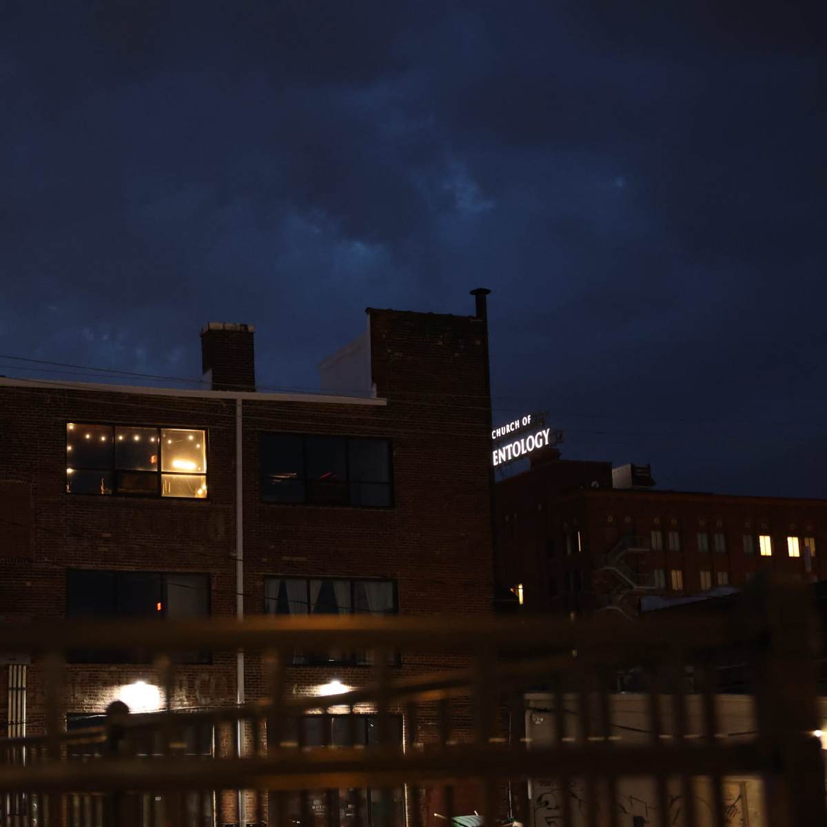 A brick building with illuminated windows stands against a darkening sky, featuring a sign that reads "College of Ethnology."