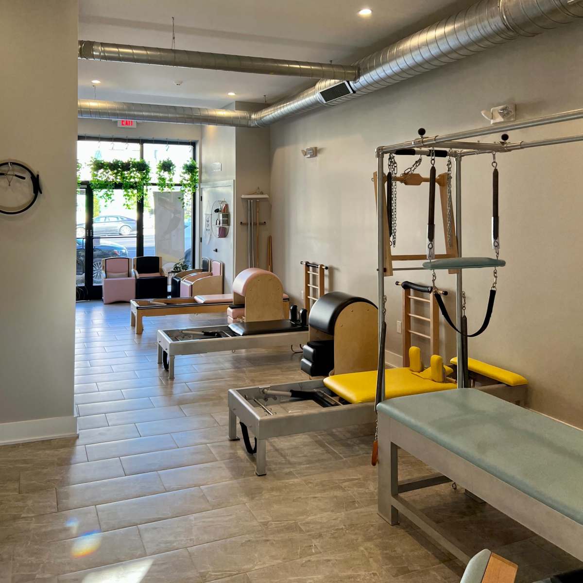 A Pilates studio featuring reformer machines, wall-mounted equipment, and large windows with natural light.