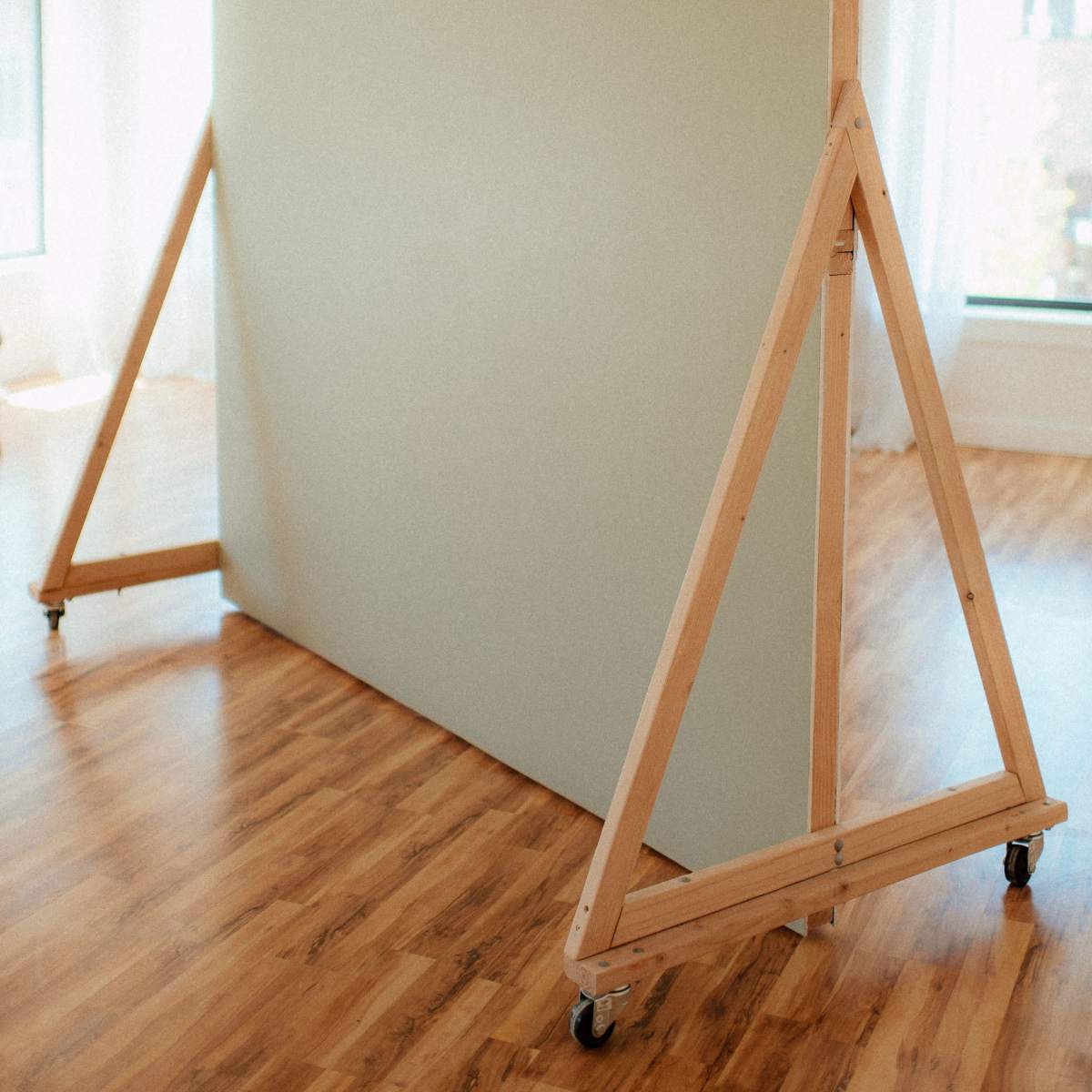 A large, portable, green partition stands on wooden supports with wheels in a well-lit room.