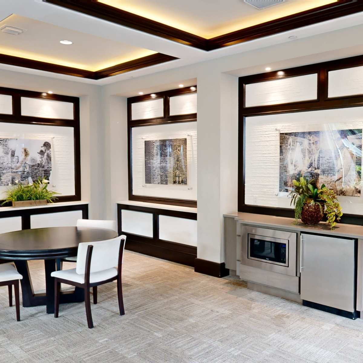 A modern interior space with a round table and chairs, framed artwork on the walls, and a built-in microwave unit.