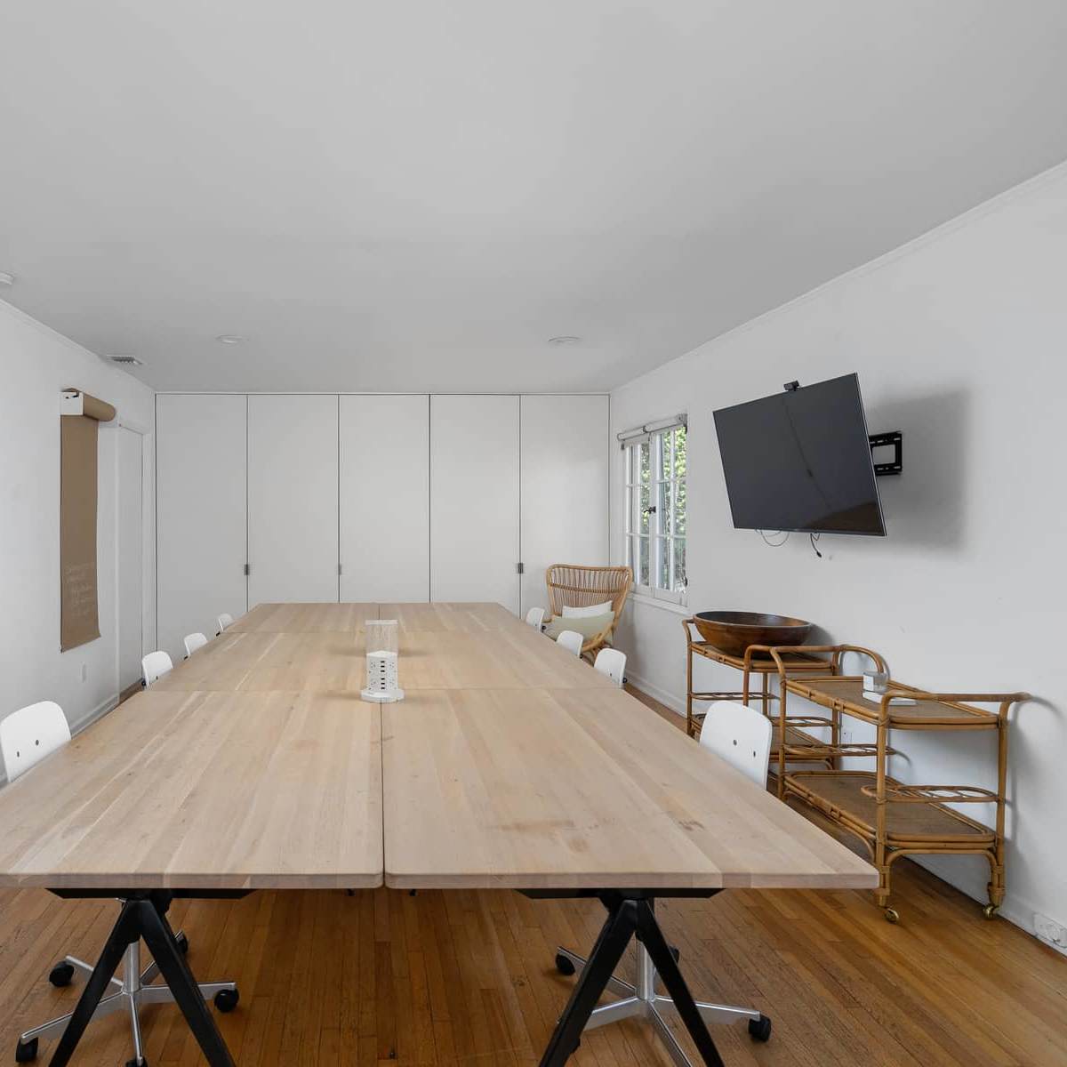 A spacious conference room with a long wooden table surrounded by white chairs and a wall-mounted television.